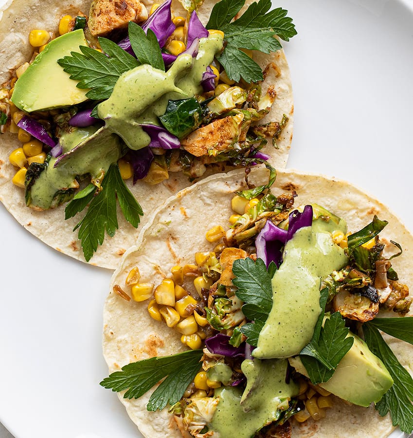 Two tacos with avocado, corn, and brussels sprouts.