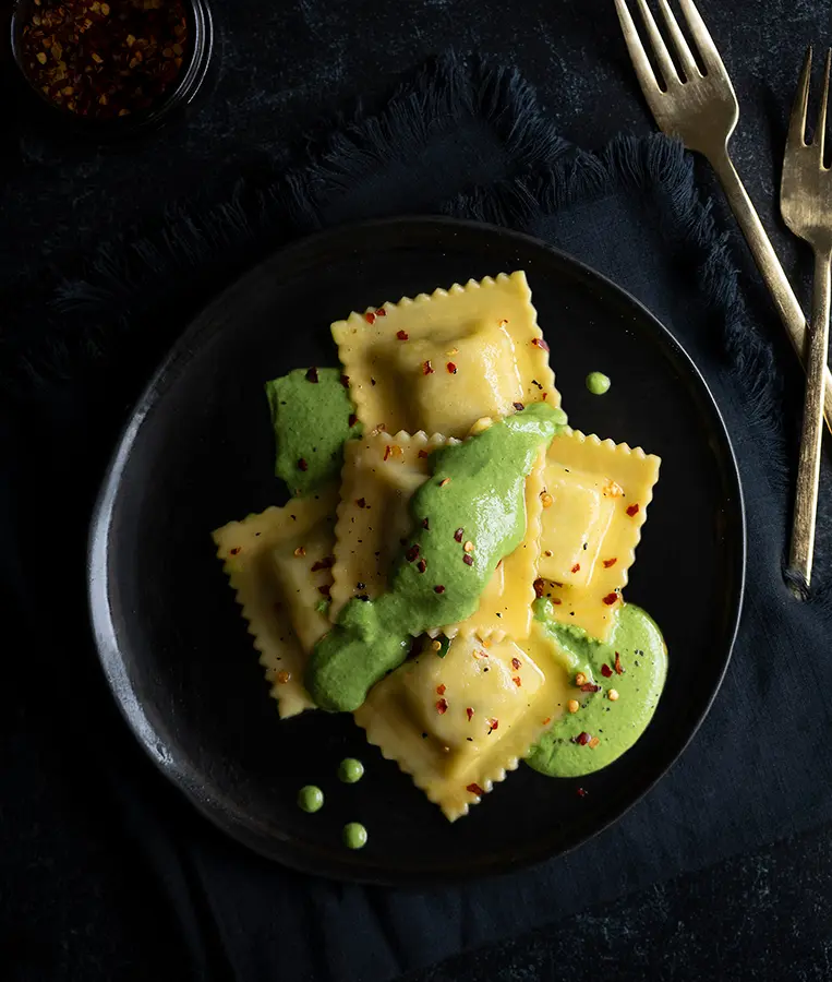 Ravioli with green sauce and red pepper flakes.