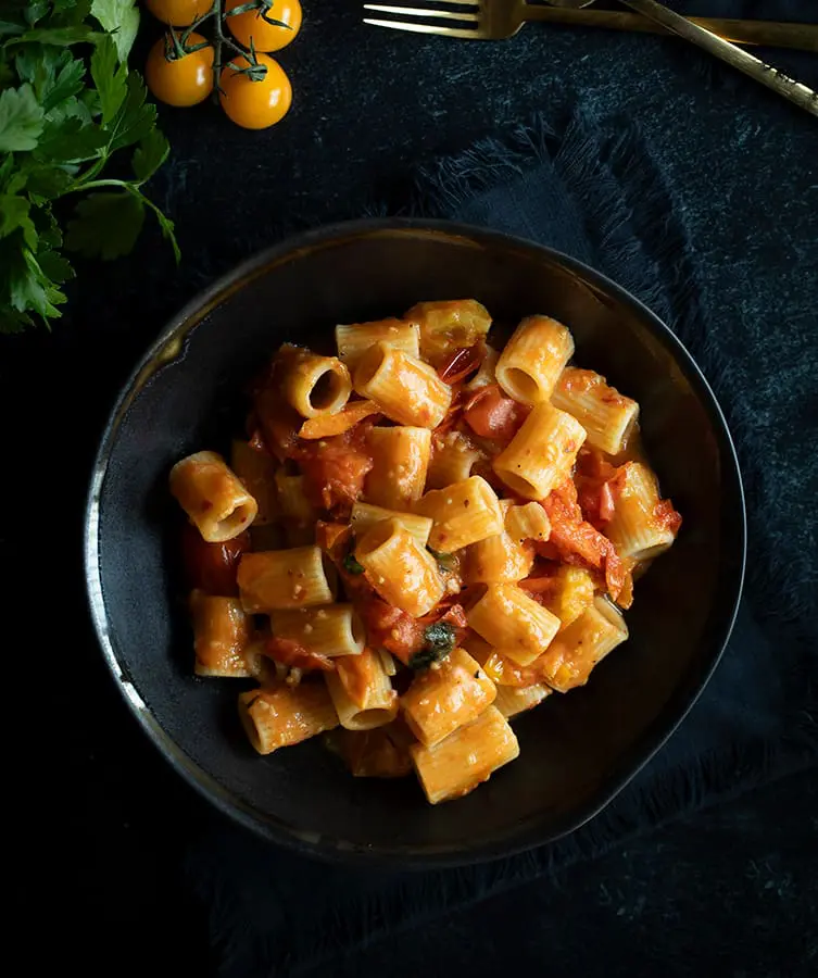 Tomato pasta in black bowl on table.